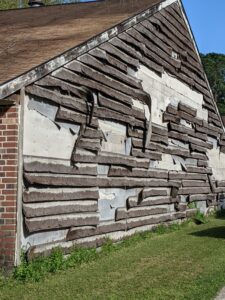 Here's an alt tag for the image: `Damaged wooden siding on building`